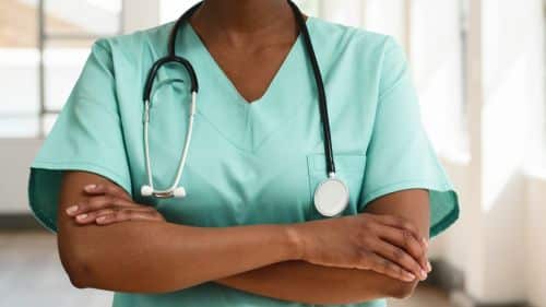 Healthcare professional crossing arms while wearing green scrubs and a stethoscope. The gesturing portrays confidence and professionalism, situated in a well-lit medical environment, symbolizing care, expertise, and dedication to patient health.